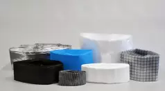Stack of folded liner foils in various colors and materials, neatly arranged. Visible variants include black, transparent, white, blue, and metallized — commonly used in pharmaceutical or chemical containment.