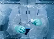 Operator handling a bottle with blue liquid inside a flexible isolator using integrated glove ports – for contamination-free work in pharmaceutical or chemical environments.
