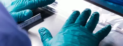 Close-up of gloved hands precisely aligning a film sheet during quality control or converting in cleanroom conditions – part of Lugaia’s single-use containment production.