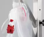 A transparent containment bag with red SafeSeal closure, attached to a vertical stainless steel bracket – part of a single-use transfer system for safe product handling.